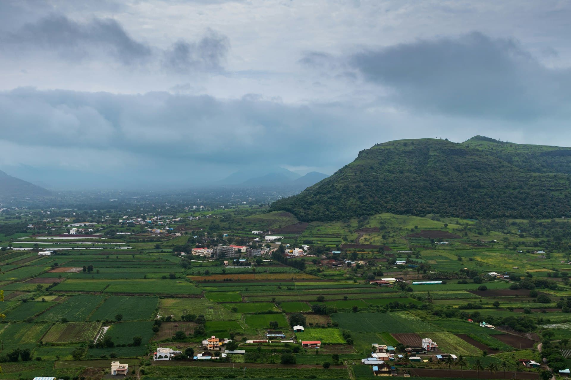 Green farm fields below a hill in rural India